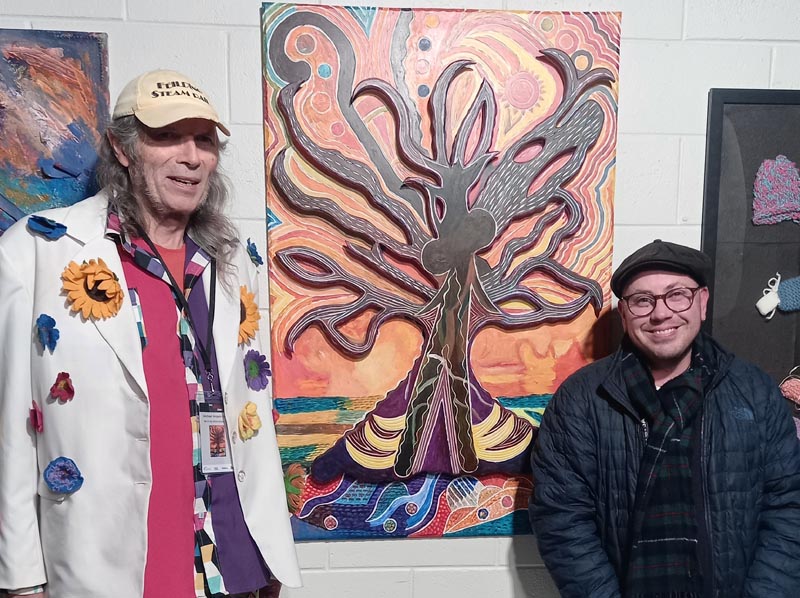 Michael and Stace stand beside Michael’s colourful painting of a large, branching tree.